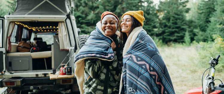 Two people wrapped in a blanket on a campsite
