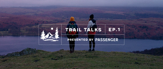 two women walking in the distance along a trail, with pink sunrise skies in front of them